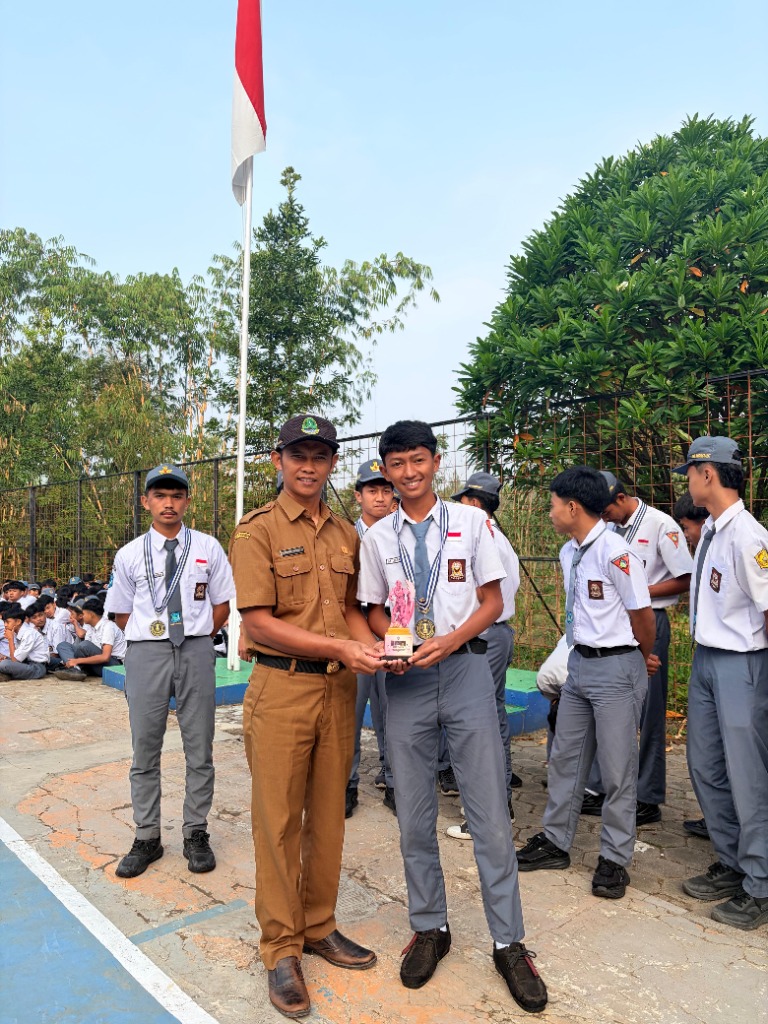 Waka Kesiswaan Ade Sandi, S.Pd. menyerahkan trofi kejuaraan futsal kepada perwakilan kapten tim siswa di lapangan SMKN 1 Rongga