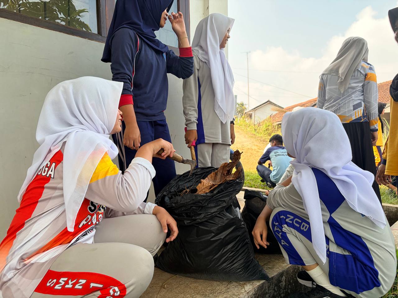 Siswi SMKN 1 Rongga mengumpulkan dedaunan kering dan sampah organik ke dalam kantong sampah besar dalam aksi ekologi