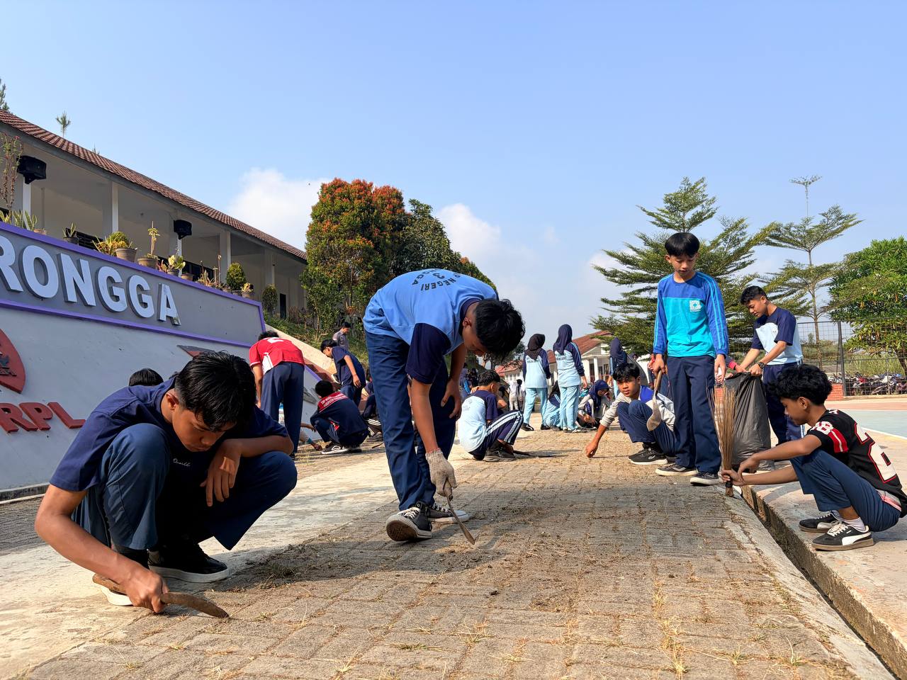 Siswa SMKN 1 Rongga berjongkok membersihkan rumput liar dan lumut di sela paving block jalan sekolah