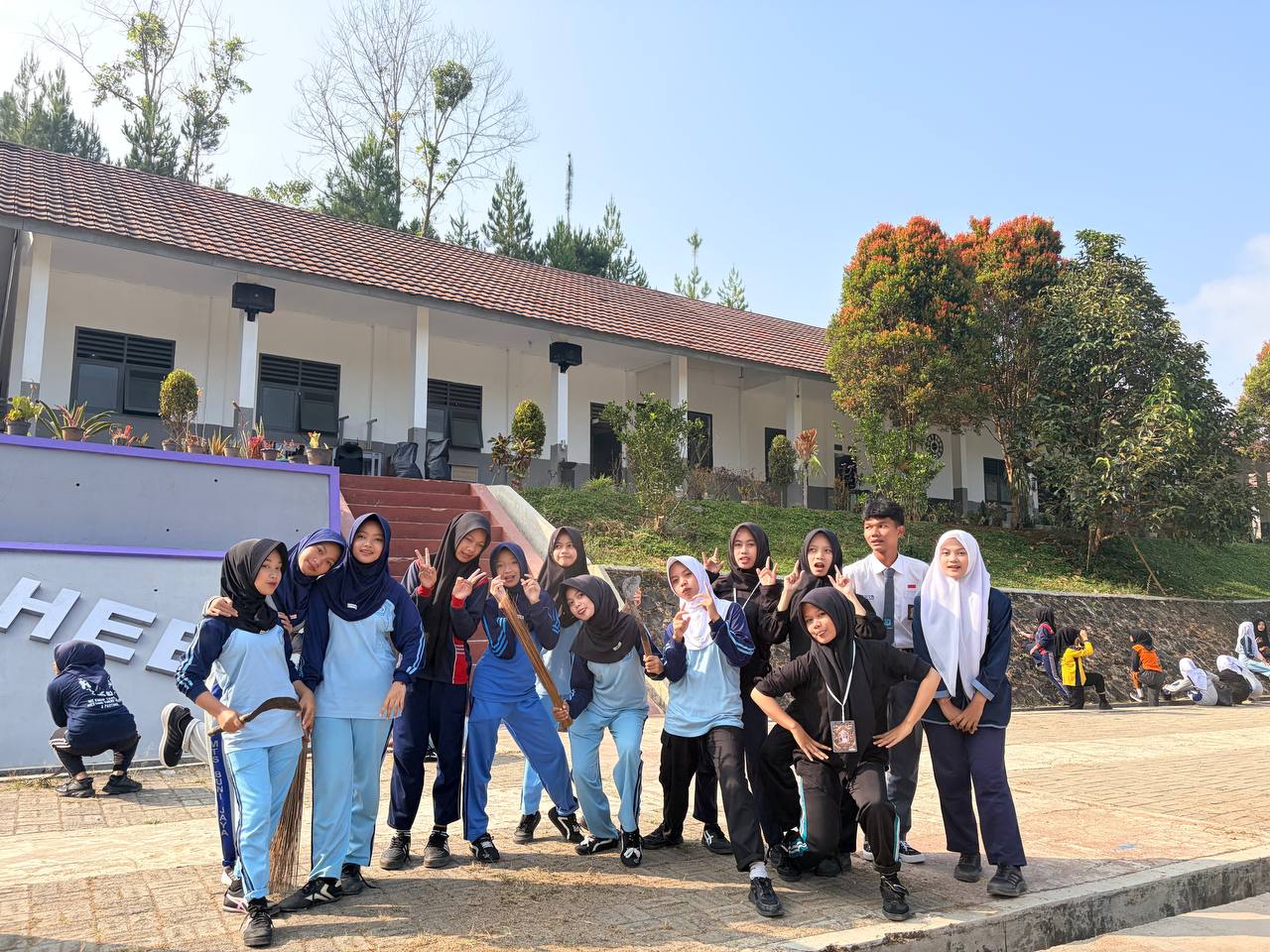 Foto bersama siswi-siswi SMKN 1 Rongga membawa sapu dan alat kerja bakti di depan tangga gedung sekolah