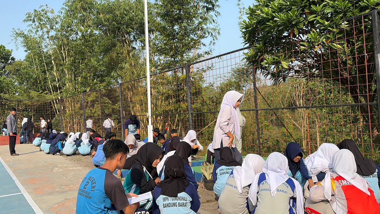 Siswa-siswi SMKN 1 Rongga duduk berjejer merapikan area tepi lapangan olahraga sekolah di dekat pagar pembatas