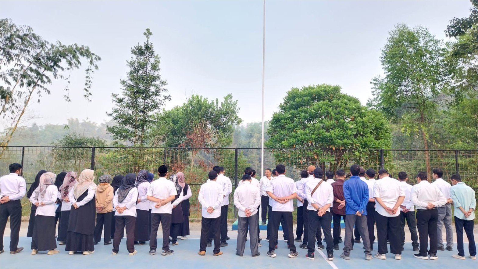 Para guru SMKN 1 Rongga mengikuti apel pembinaan menghadap pembina di lapangan dengan latar pepohonan