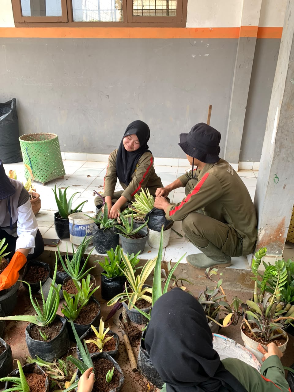 Sekelompok siswa ATPH SMKN 1 Rongga tersenyum ceria sambil mengerjakan praktikum media tanam di koridor sekolah