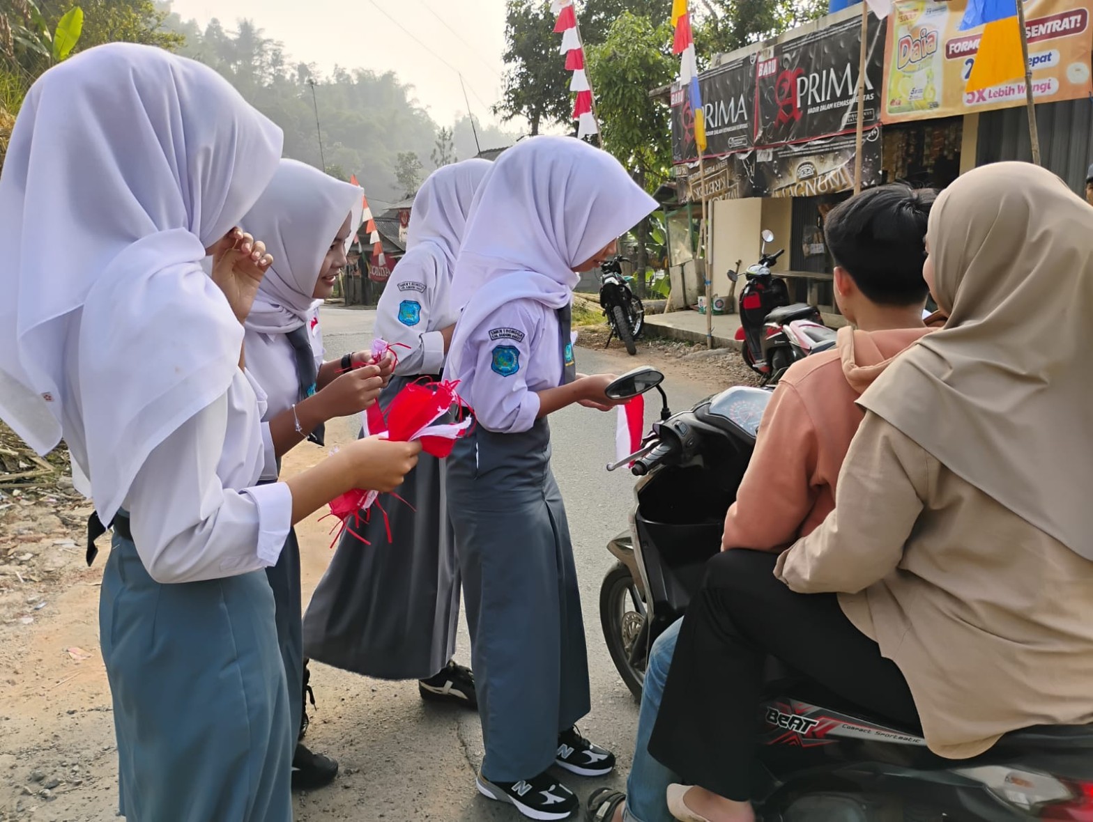 Siswi SMKN 1 Rongga membagikan bendera merah putih kecil kepada pengendara motor di jalan depan sekolah