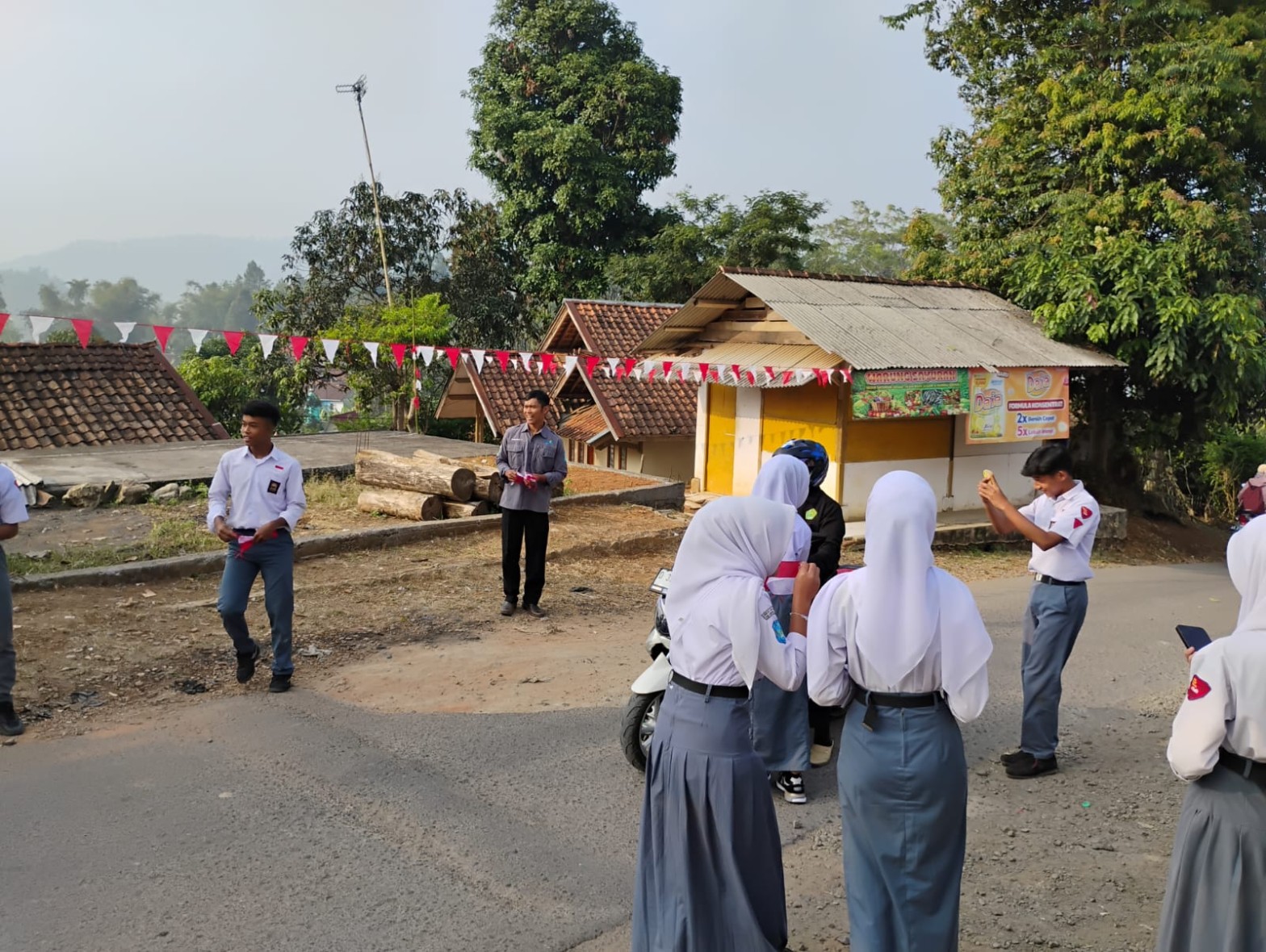 Siswa SMKN 1 Rongga berdiri di pinggir jalan membagikan bendera merah putih kepada pengendara motor yang melintas