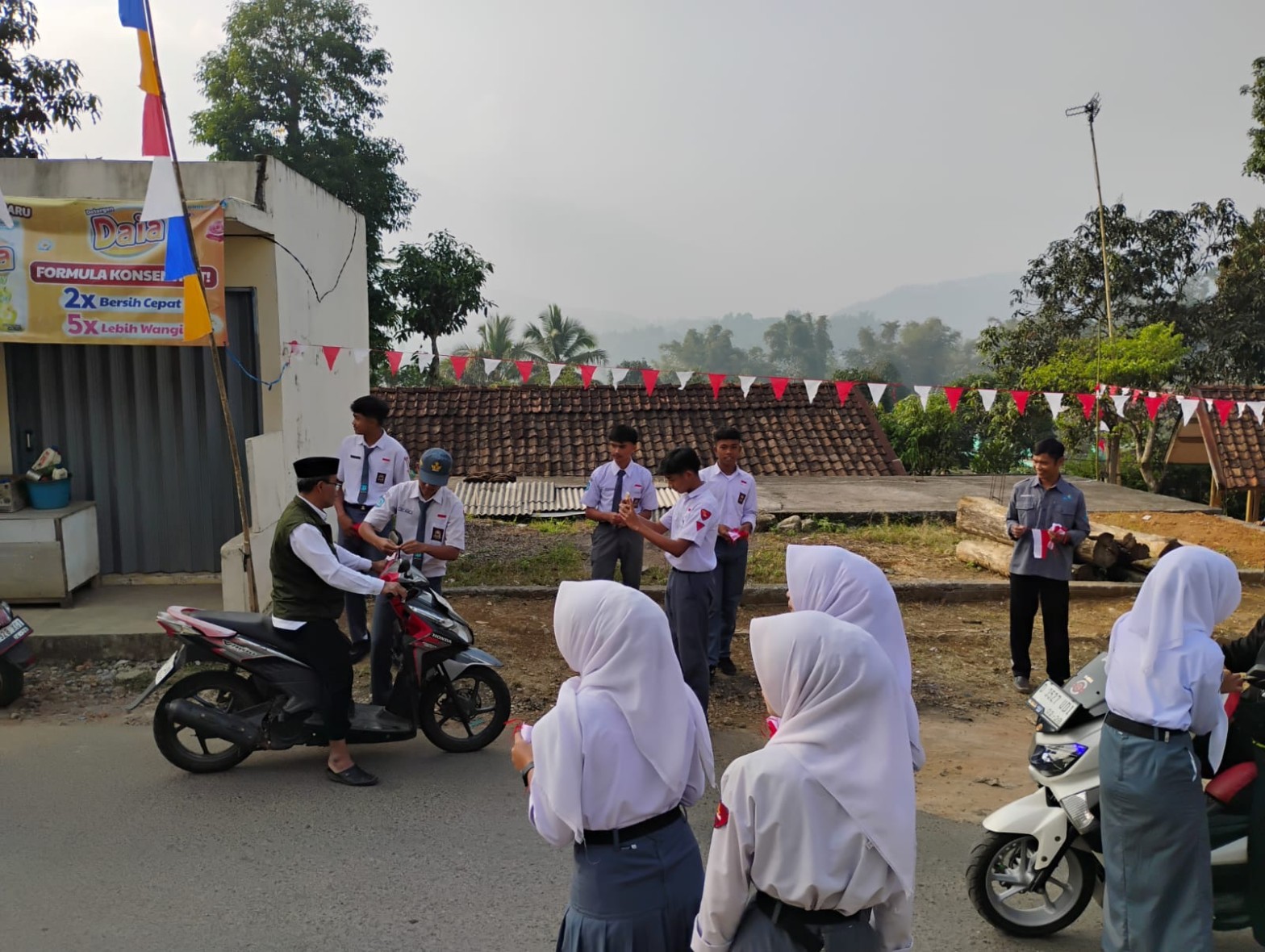 Siswa SMKN 1 Rongga berbaris di jalan yang dihiasi umbul-umbul merah putih sambil membagikan bendera kepada pengendara