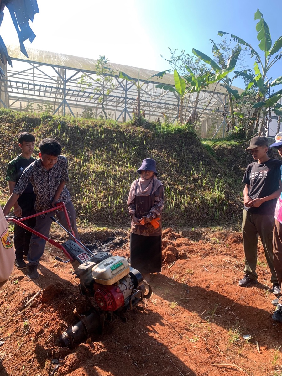 Agnia Fila Anisa, S.P. mendampingi siswa saat praktik langsung menggemburkan lahan menggunakan mesin kultivator