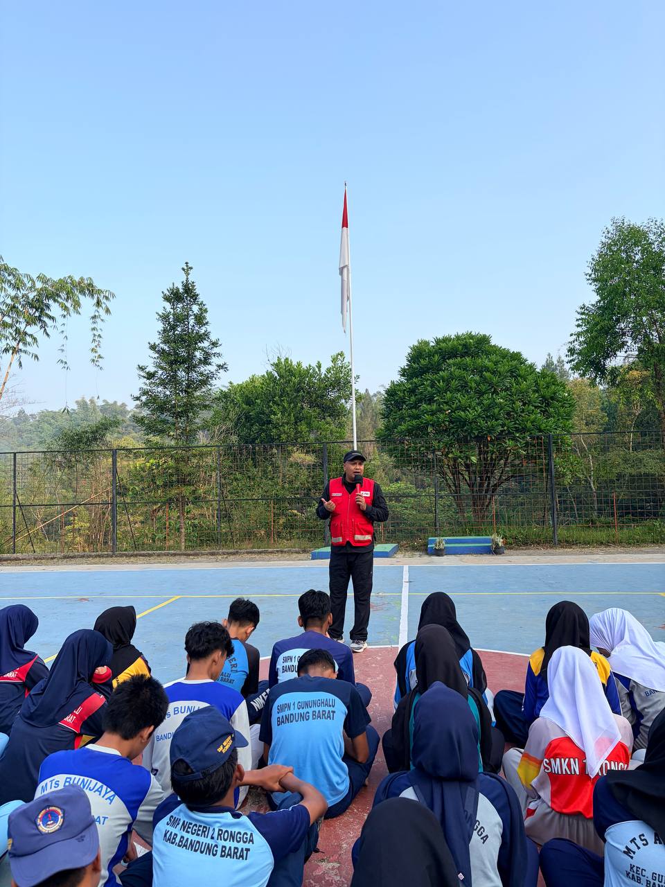 Instruktur PMI berbicara di lapangan upacara SMKN 1 Rongga di bawah tiang bendera Merah Putih disimak siswa