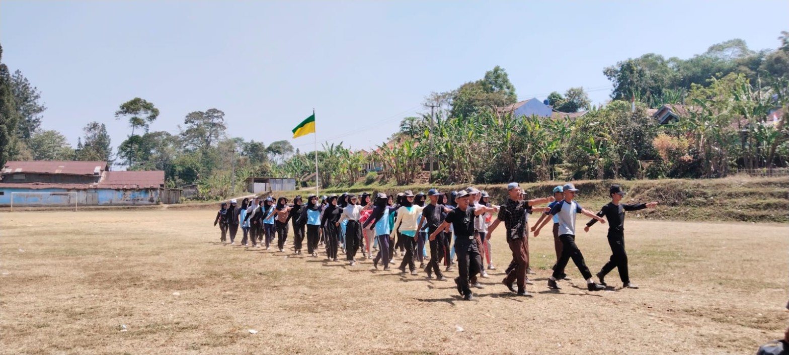Formasi panjang anggota Paskibra SMKN 1 Rongga berbaris melintasi Lapangan Kecamatan Rongga dengan bendera berkibar di latar