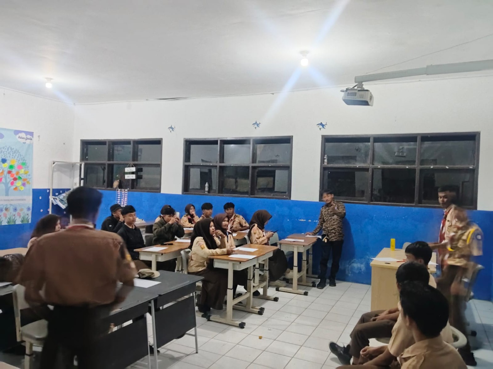 Peserta Pramuka berseragam duduk di bangku kelas mengikuti sesi evaluasi dan materi malam perkemahan HUT Pramuka