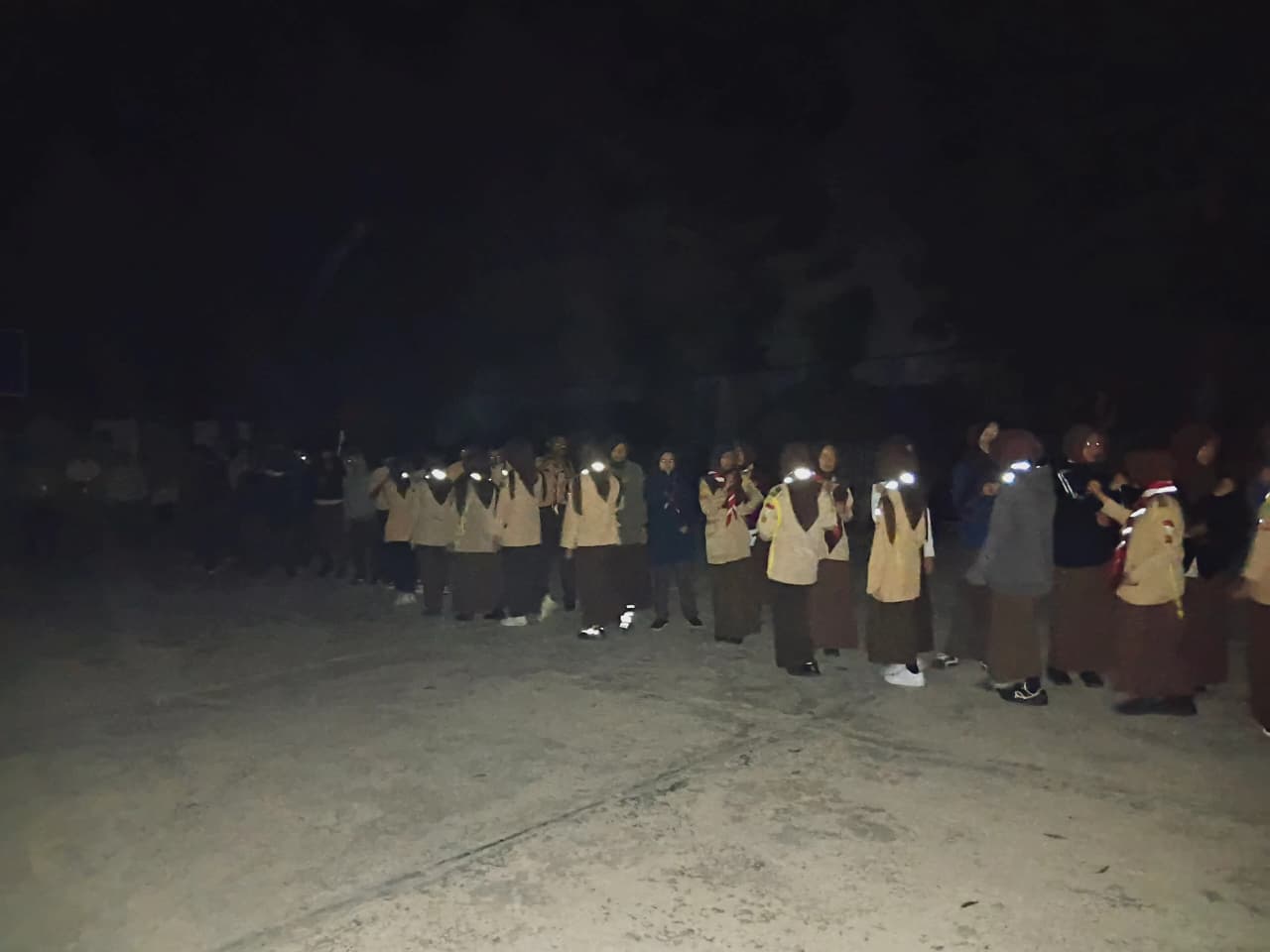 Barisan panjang peserta Pramuka berjalan pada malam hari dengan senter kepala menyala dalam kegiatan longmarch perkemahan HUT Pramuka