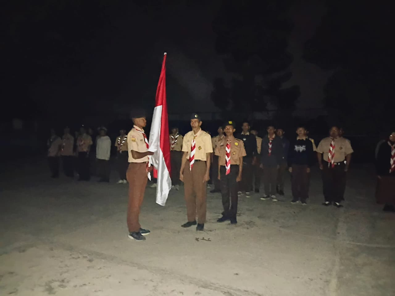 Petugas pramuka mengibarkan bendera Merah Putih pada upacara malam di lapangan perkemahan HUT Pramuka