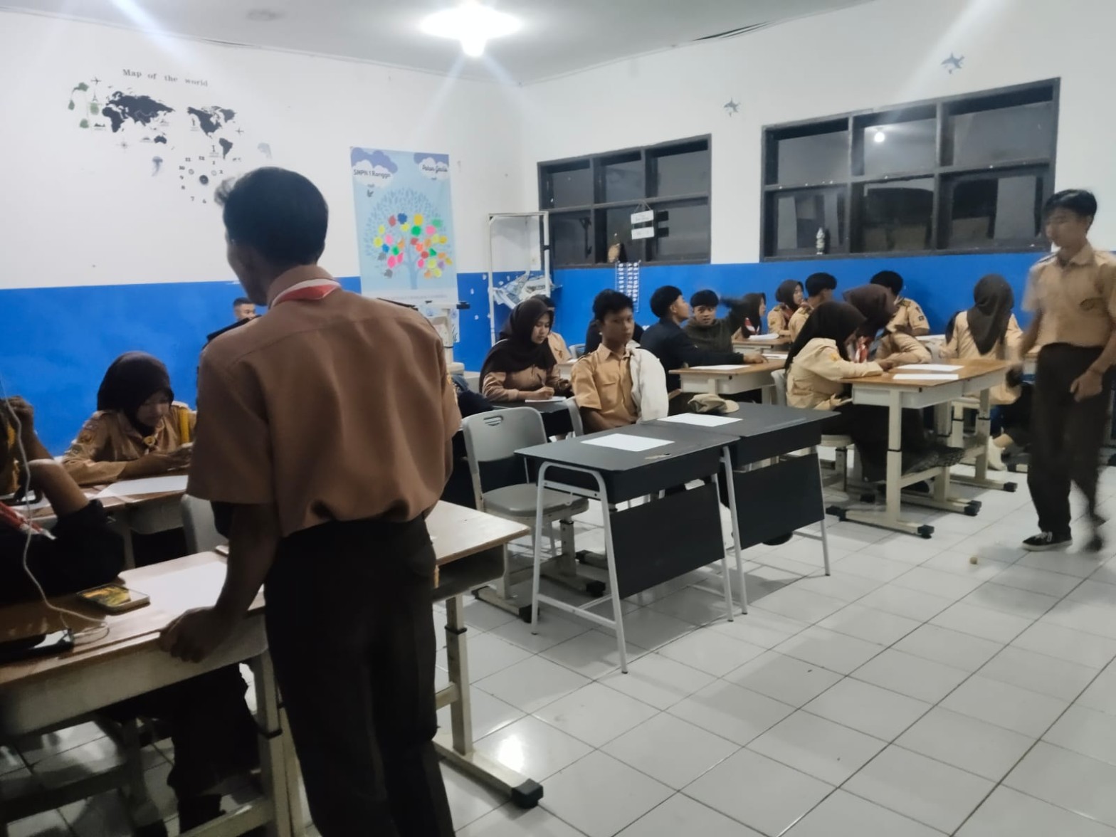 Peserta Pramuka duduk berkelompok di kelas sambil mengerjakan tugas pada sesi malam perkemahan HUT Pramuka