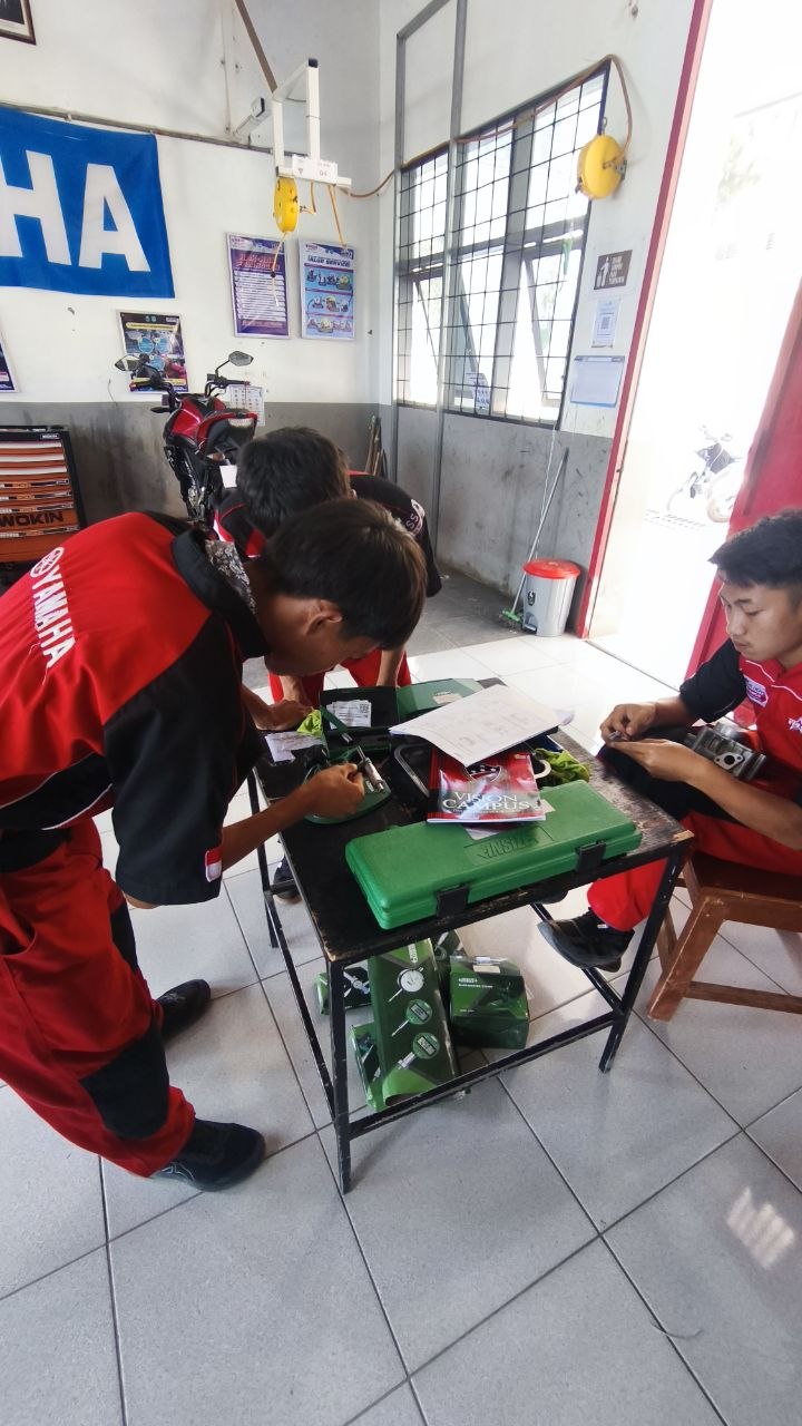 Siswa TSM berseragam Yamaha melakukan pengukuran komponen mesin menggunakan alat ukur presisi di meja kerja bengkel