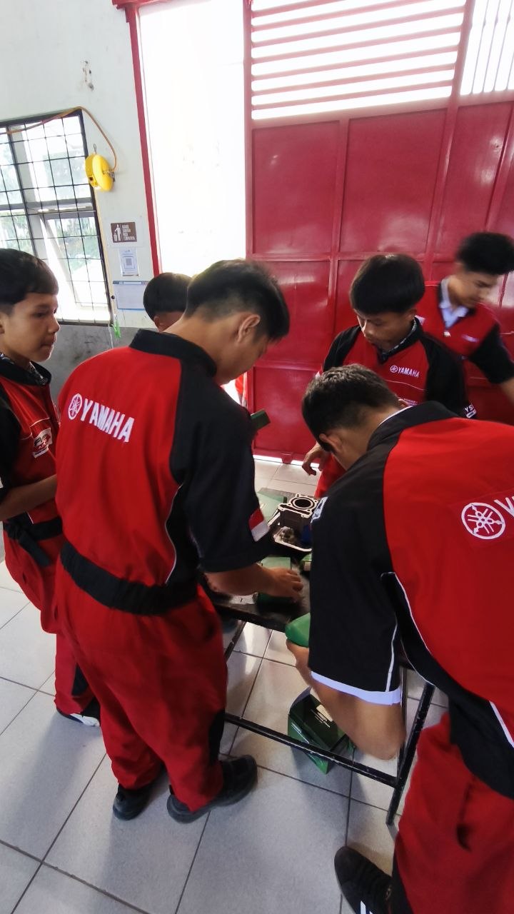 Siswa TSM SMKN 1 Rongga berkumpul memeriksa komponen silinder mesin di dekat pintu bengkel bercat merah