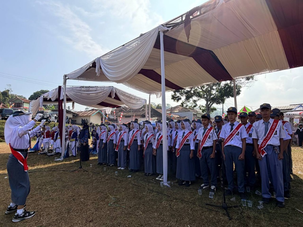 Tim Paduan Suara SMKN 1 Rongga Choir berbaris rapi di bawah tenda dengan selempang merah dipimpin oleh seorang dirigen saat menyanyikan lagu kemerdekaan
